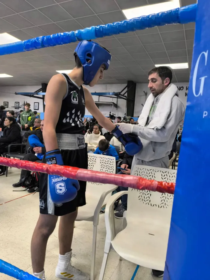 Entrenador ajustando los guantes azules a un joven boxeador del club con casco antes de subir al ring en Lugo