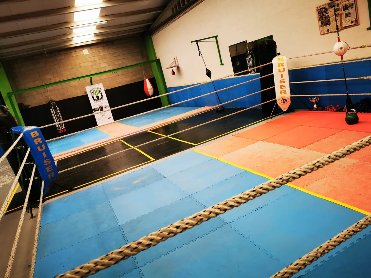 Ring de boxeo del box de Turoqua visto desde las cuerdas, con los sacos y los trofeos del club al fondo